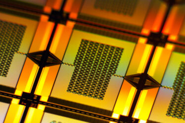 A yellow-lit closeup zooms in on one tiny, rectangular amplifier on the wafer. It has a chain-like rectangular grid in center that connects to the left and right edges of the wafer.