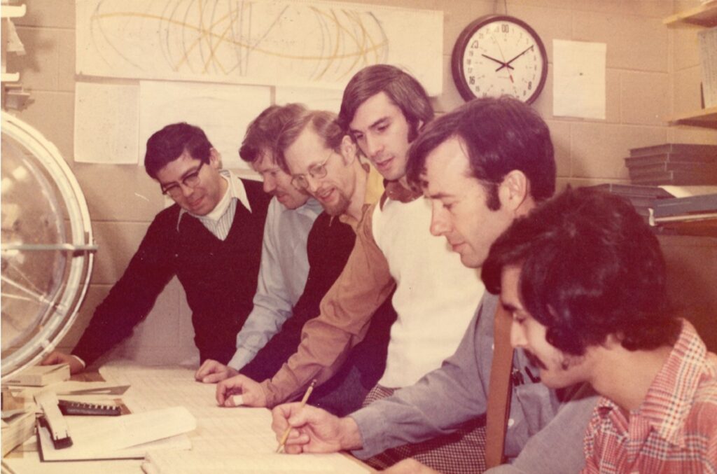 group of six men stand by desk