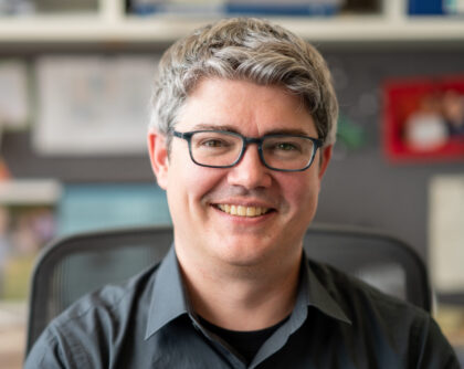 Professor Michael McDonald smiles while sitting at his desk, with blurry office background.