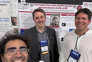 three people pose in front of physics posters