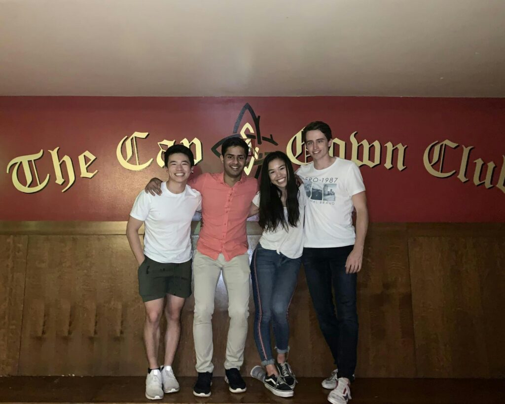 Three friends pose with Minh-Thi in front of The Cap & Gown Club sign