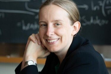 Tracy Slatyer poses in front of blackboard covered in physics equations